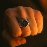 Fist wearing a silver ring with a dark stone on a dark background
