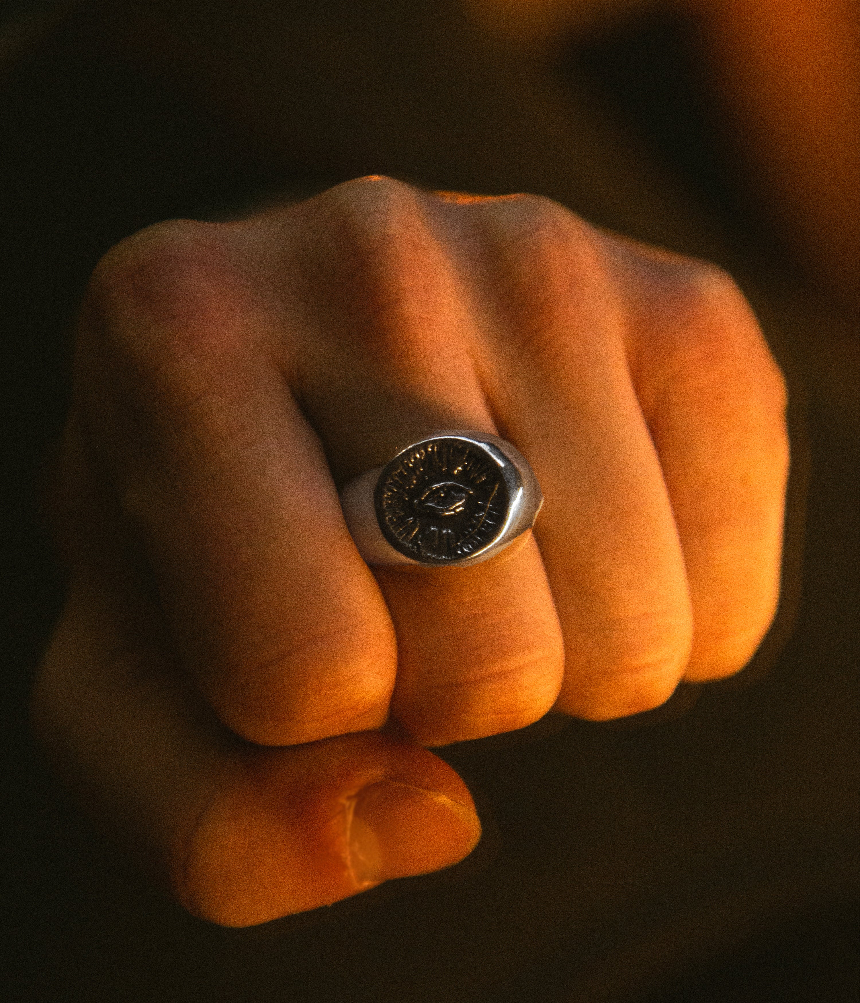 Fist wearing a silver ring with a dark stone on a dark background