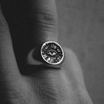 Silver ring with eye design on a finger against a dark background