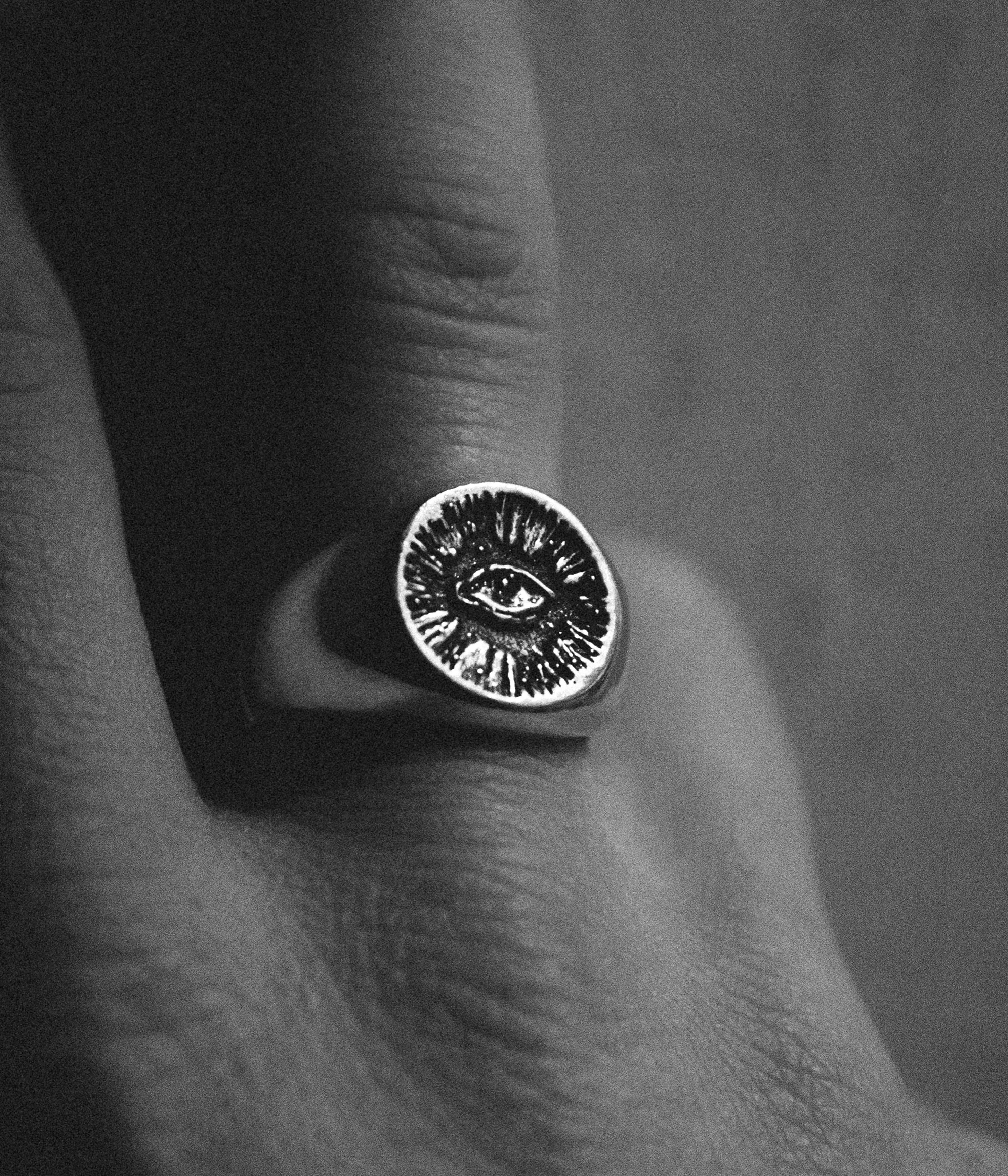 Silver ring with eye design on a finger against a dark background
