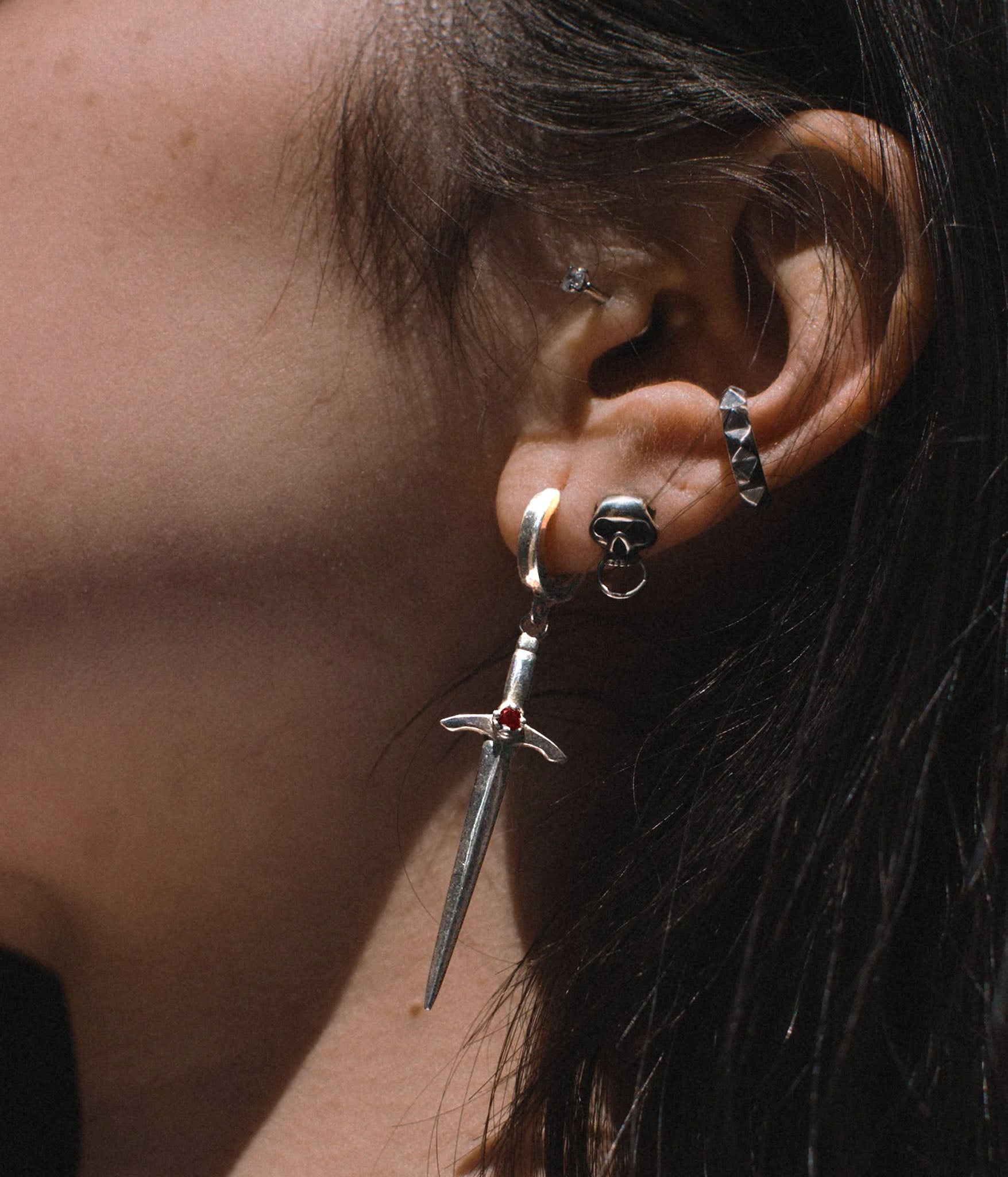 Sterling silver sword earring worn on pierced ear – dagger-shaped drop with red gemstone detail styled with mixed metal earrings