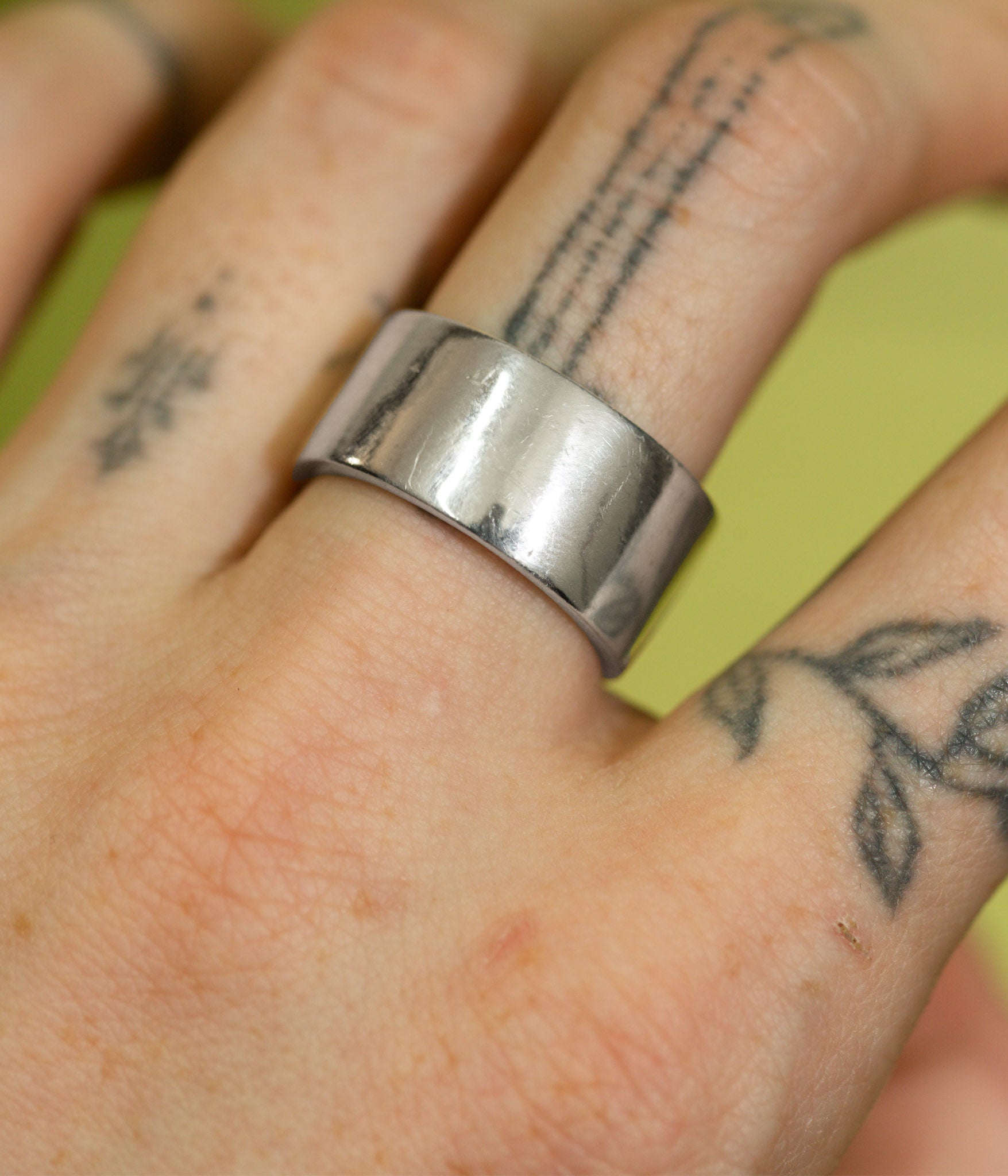 Silver ring on a finger with tattoos against a green background