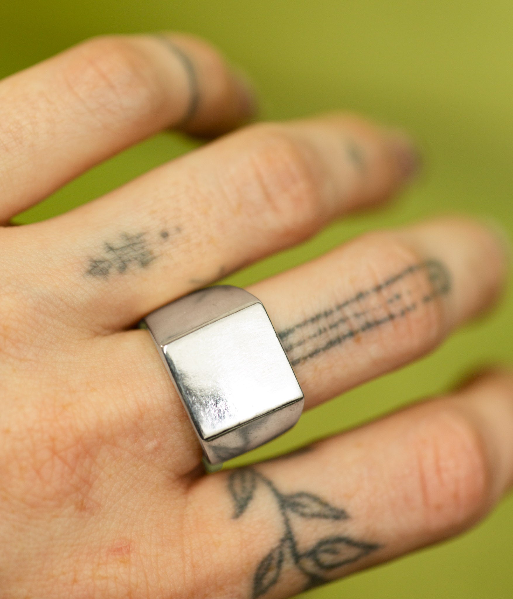 Hand wearing a silver ring with tattoos on a green background