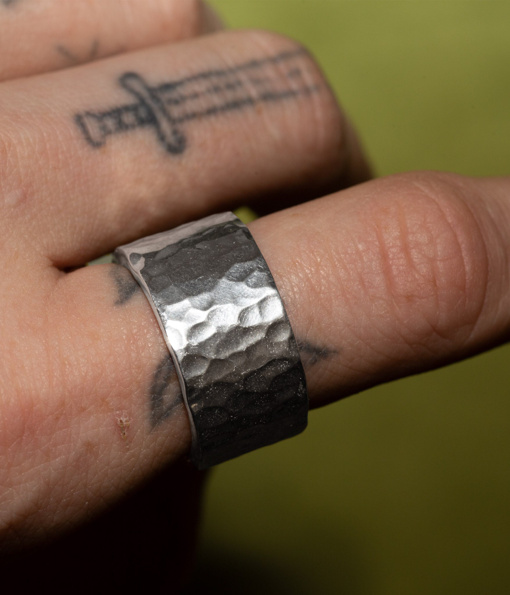 Hand wearing a textured silver ring with a blurred green background