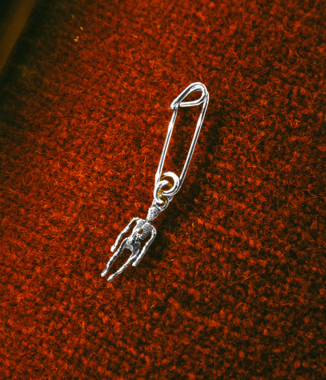 Silver safety pin with a small figure attached on a textured brown surface