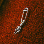 Silver safety pin with a small figure attached on a textured brown surface