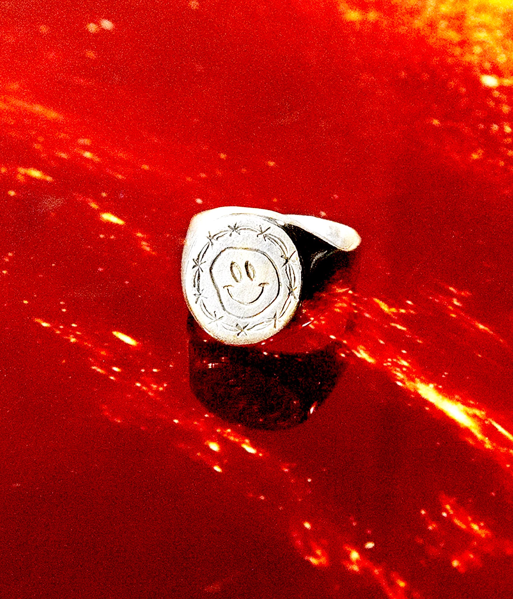 Silver ring with a smiley face design on a red background