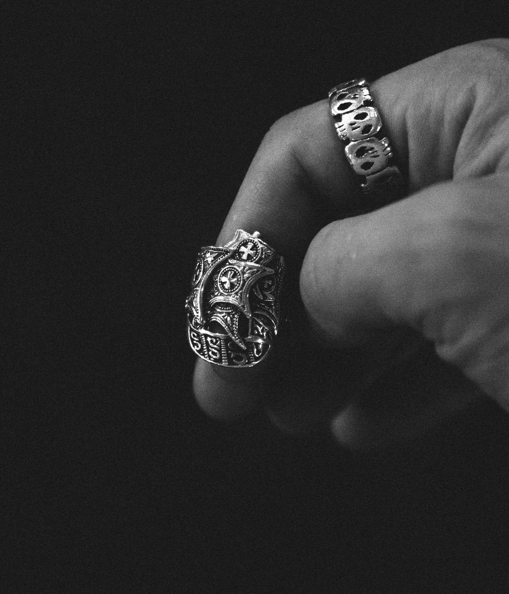 Close-up of a hand wearing two ornate silver rings on a black background