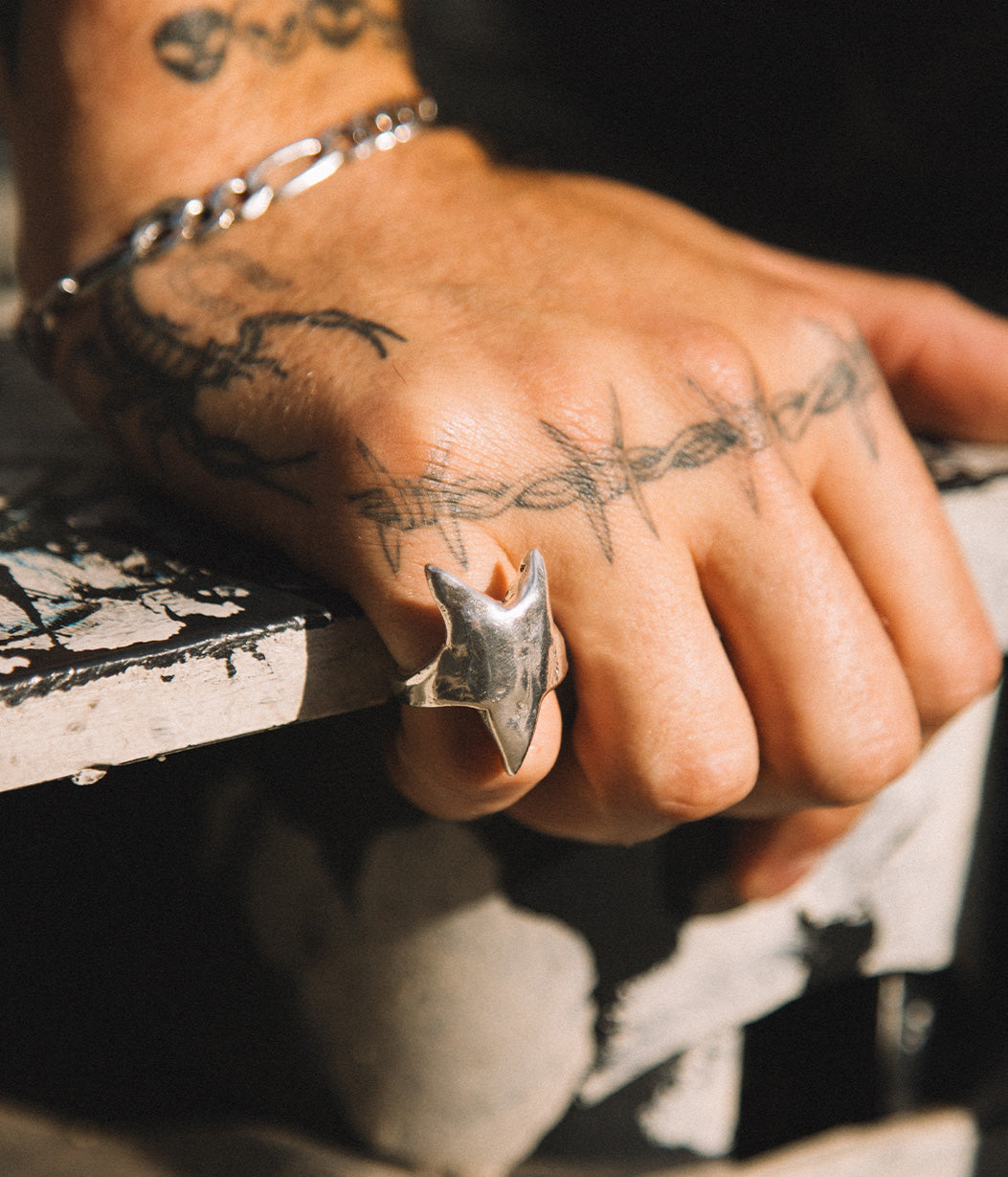 Hand with tattoos wearing a silver ring on a textured surface