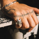 Hand with tattoos wearing a silver ring on a textured surface