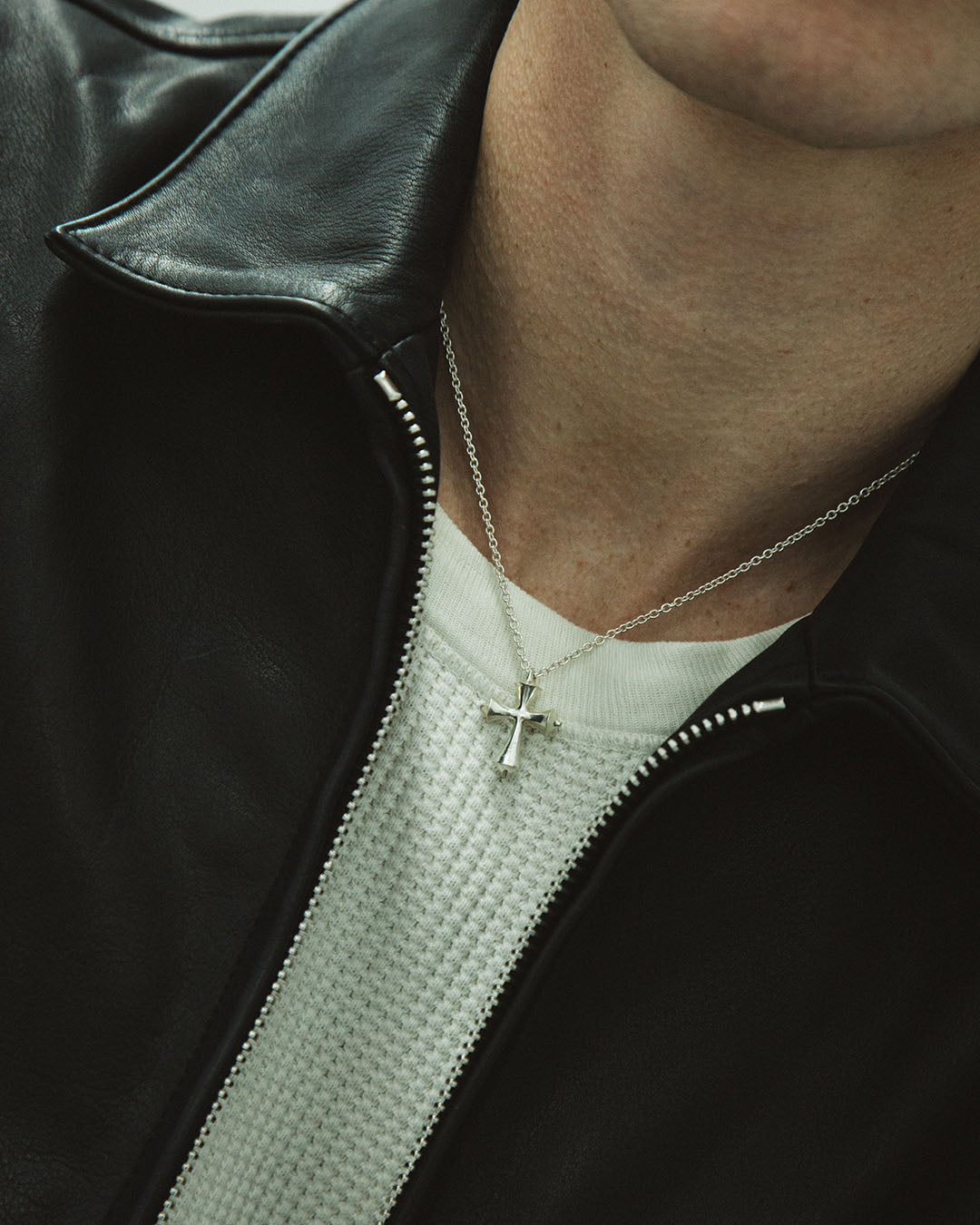 Person wearing a black leather jacket with a cross necklace.