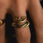 Gold snake-shaped ring on a finger with a blurred background