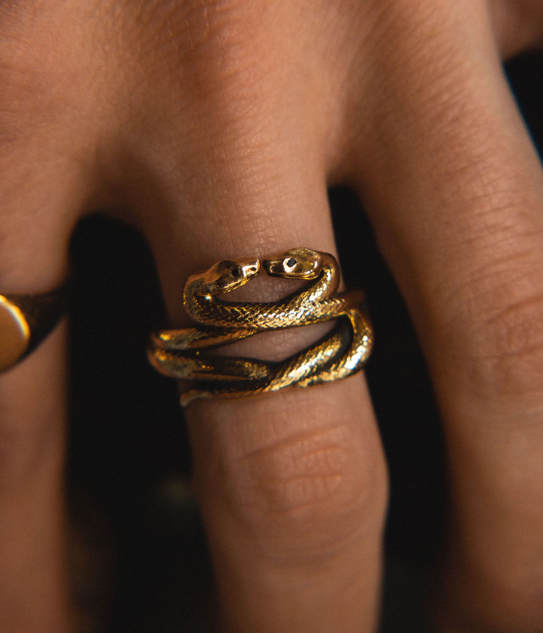 Gold snake-shaped ring on a finger with a blurred background