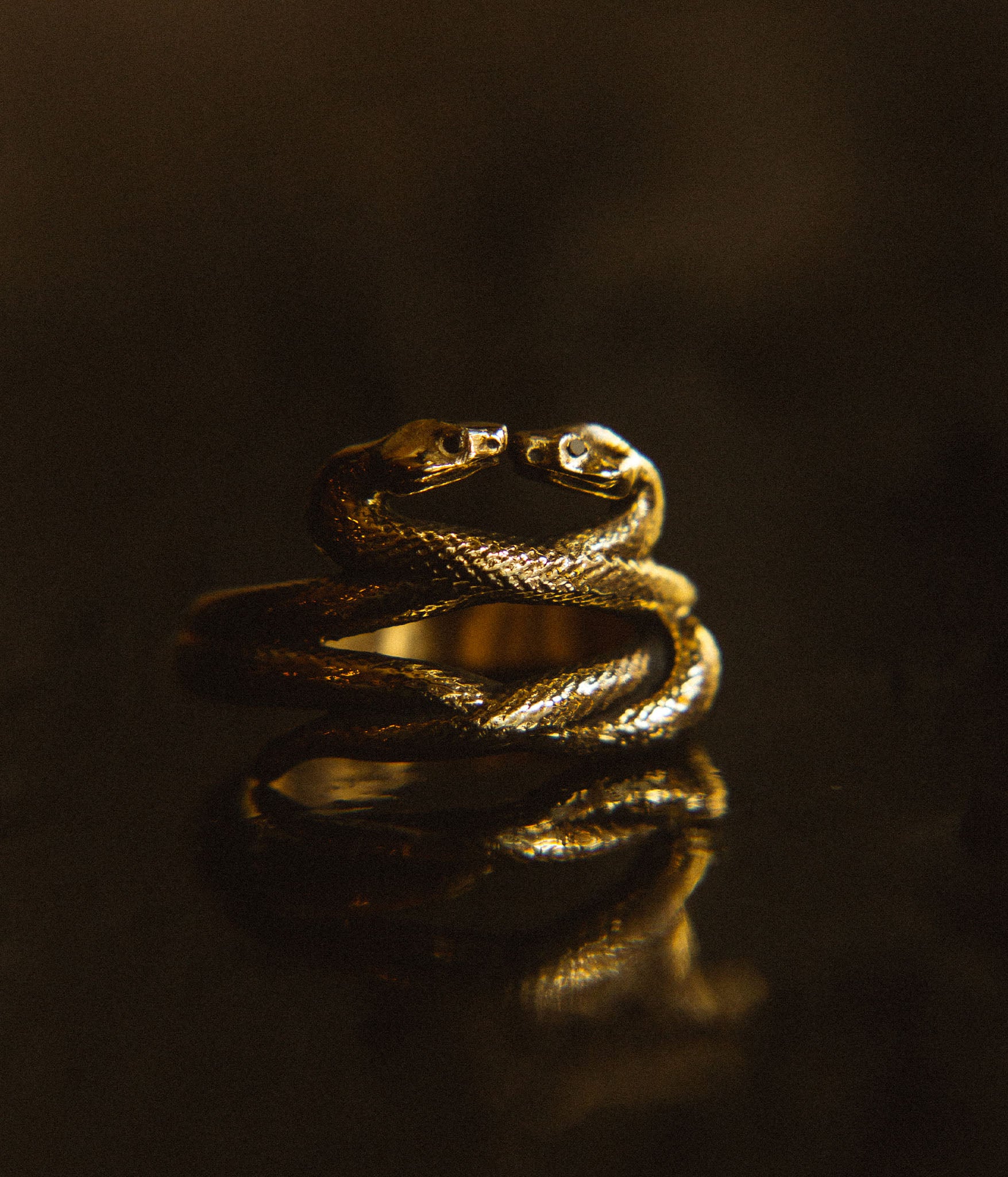 Gold snake-shaped ring on a reflective surface with a dark background