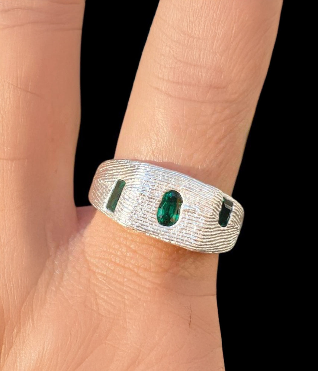 Silver ring with green gemstones on a person's finger against a black background
