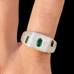 Silver ring with green gemstones on a person's finger against a black background