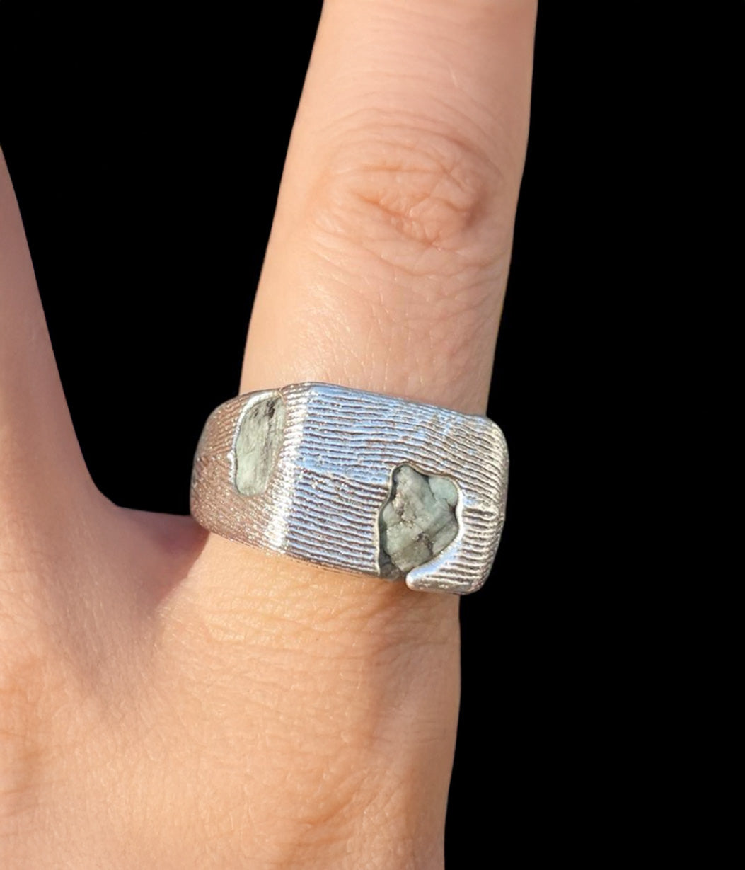 Silver ring with embedded stones on a finger against a black background