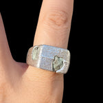 Silver ring with embedded stones on a finger against a black background