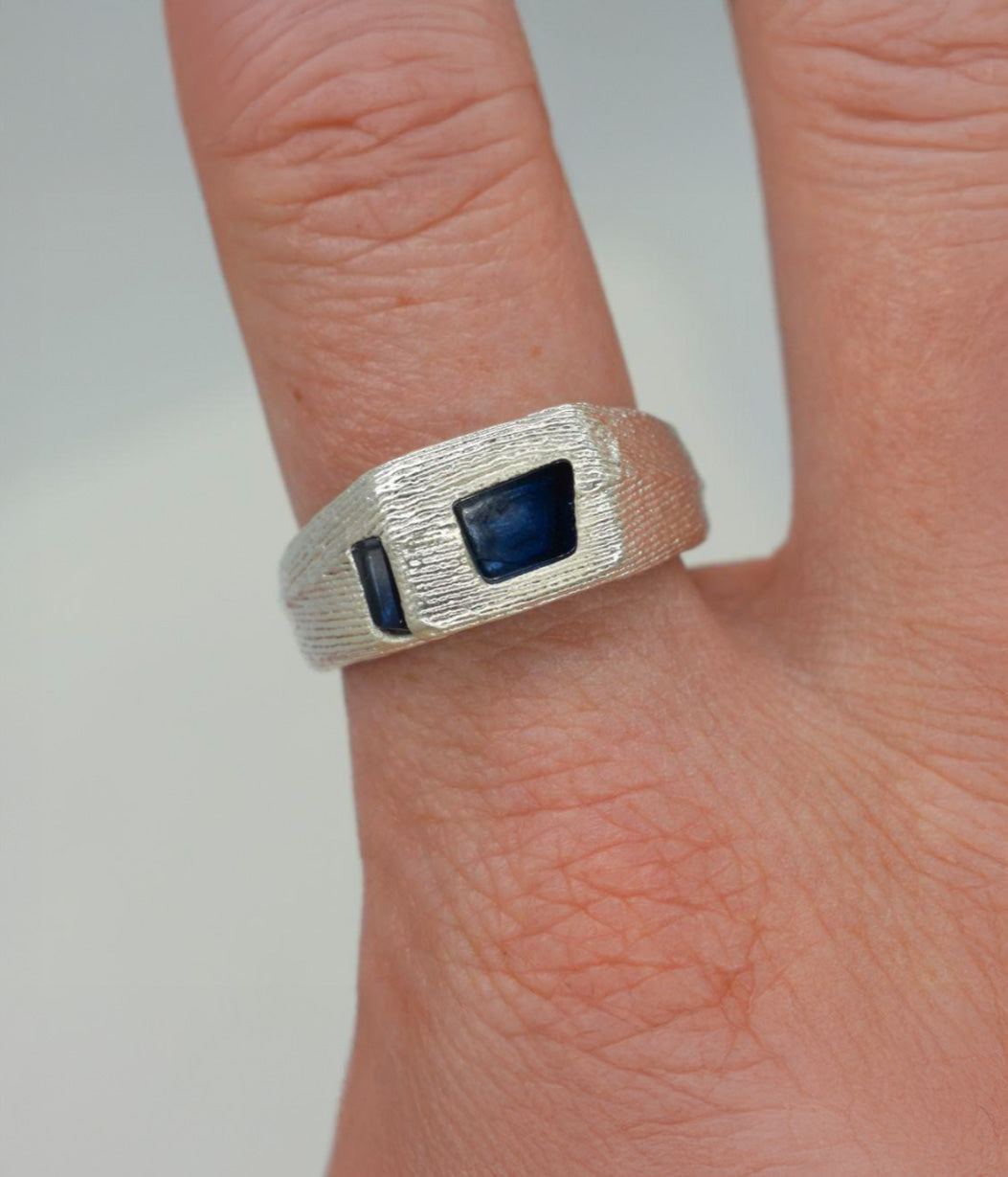Silver ring with a blue stone on a finger against a neutral background