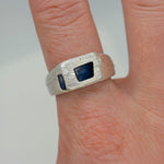 Silver ring with a blue stone on a finger against a neutral background