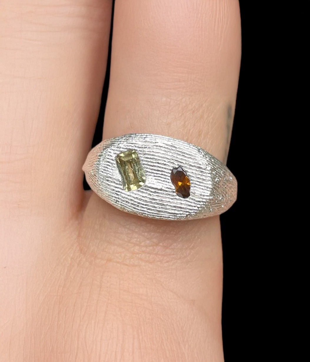 Silver ring with green and brown gemstones on a finger against a black background