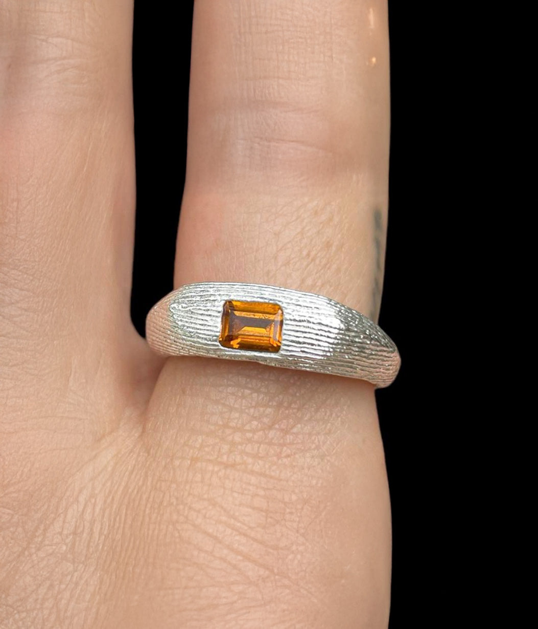 Silver ring with a rectangular orange gemstone on a finger against a black background
