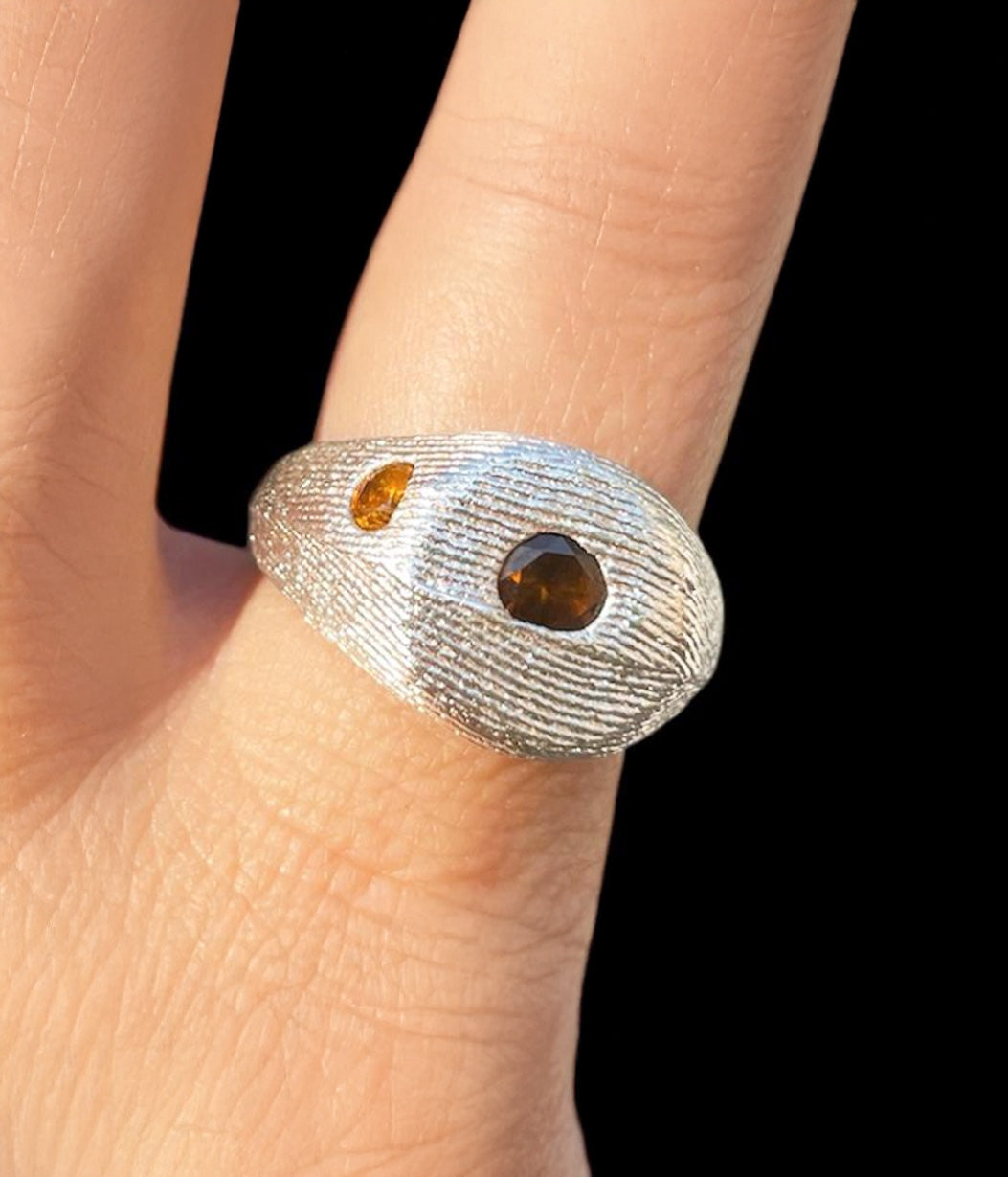 Silver ring with embedded stones on a finger against a black background