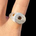 Silver ring with embedded stones on a finger against a black background