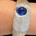 Silver ring with a blue stone on a finger