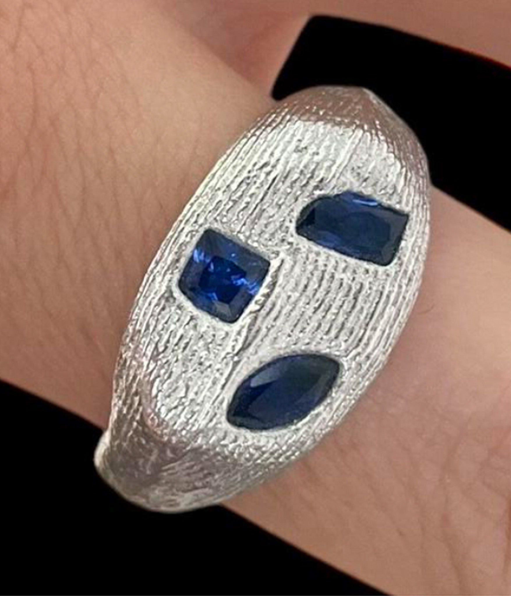 Silver bracelet with blue stones on a wrist against a black background