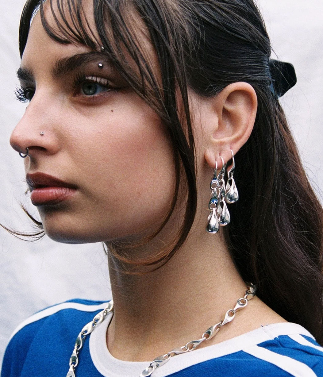 Close-up of a person wearing silver earrings and a necklace against a neutral background
