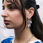 Close-up of a person wearing silver earrings and a necklace against a neutral background