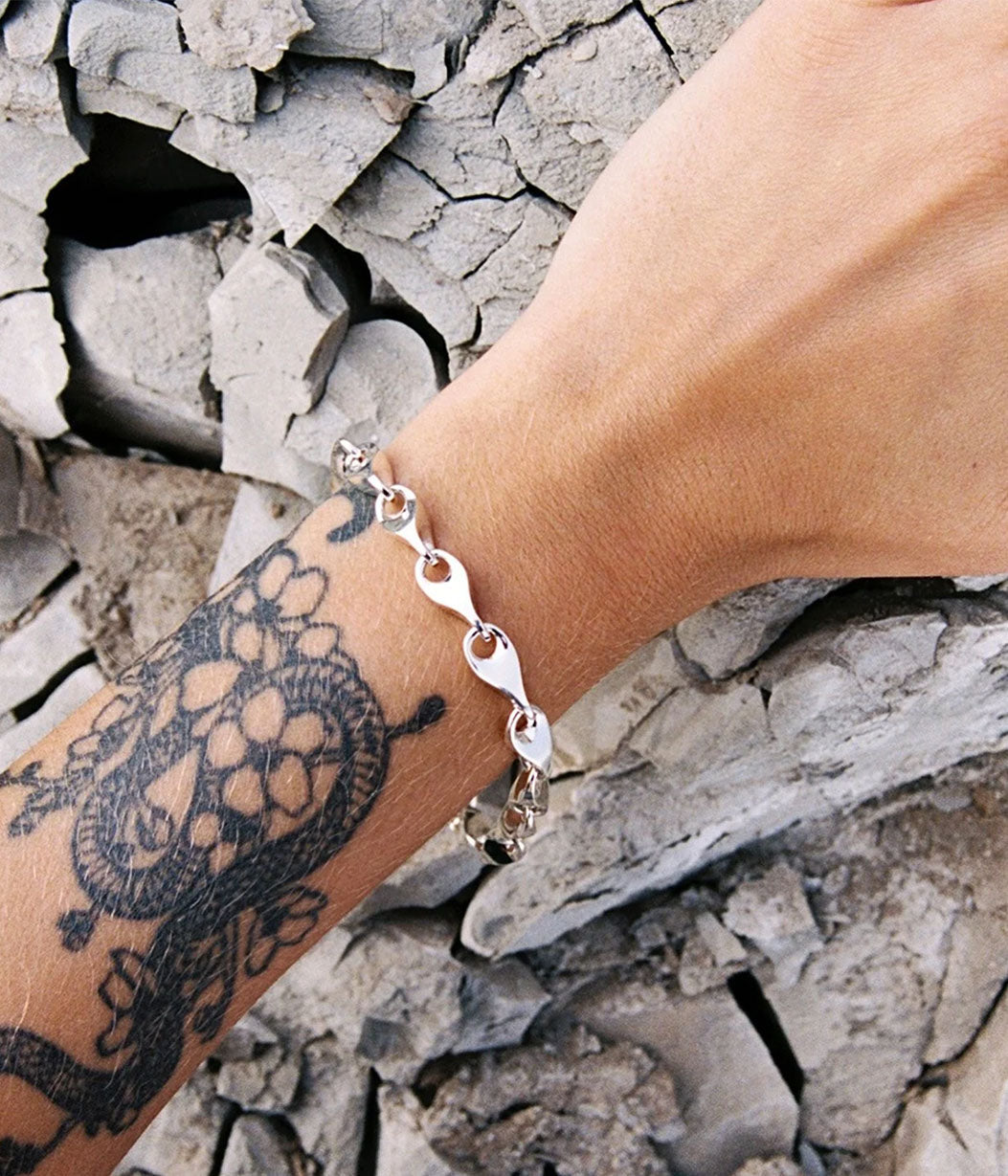 Silver bracelet on a wrist with a tattoo against a stone wall background