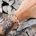 Silver bracelet on a wrist with a tattoo against a stone wall background