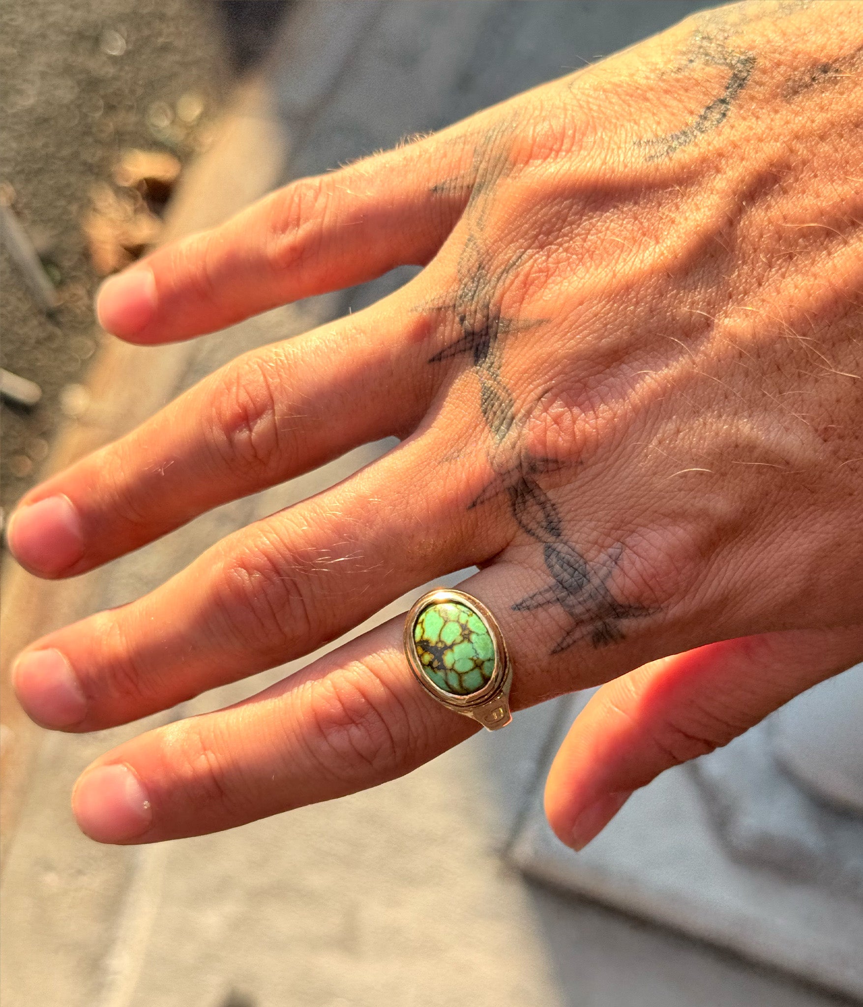 Hand wearing a ring with a green stone, set against a blurred background