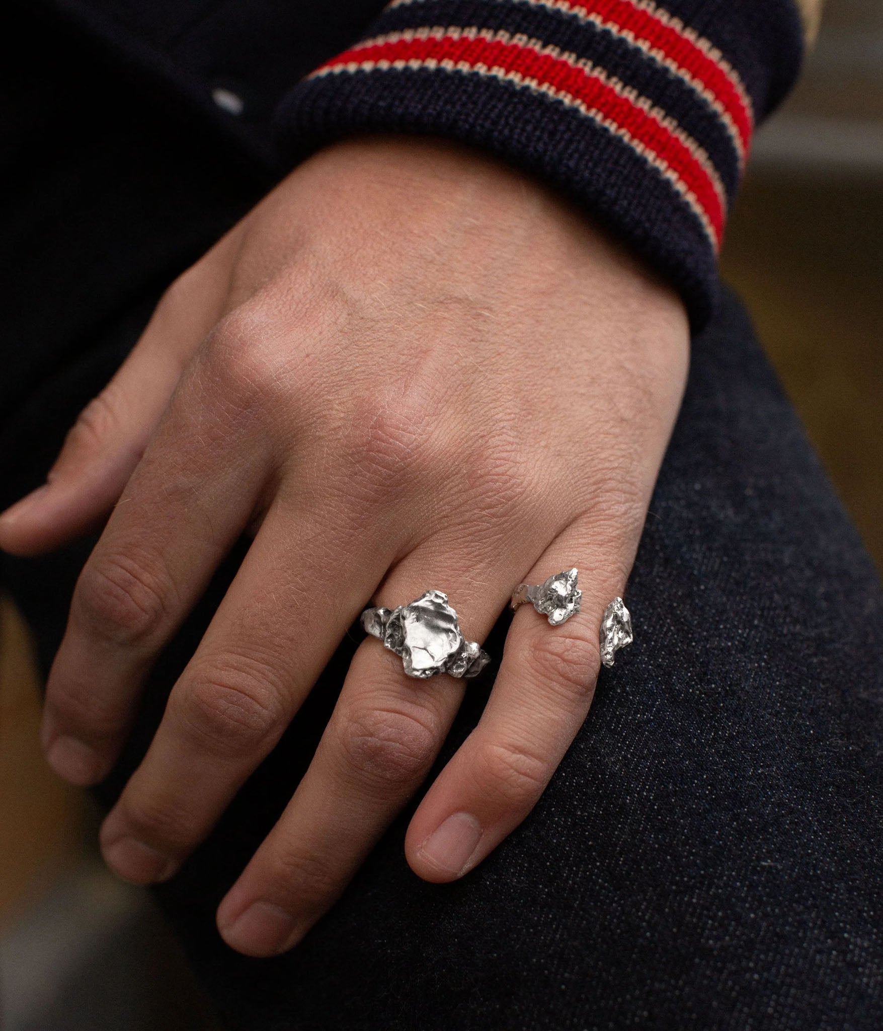 Hand wearing two silver rings on a dark background
