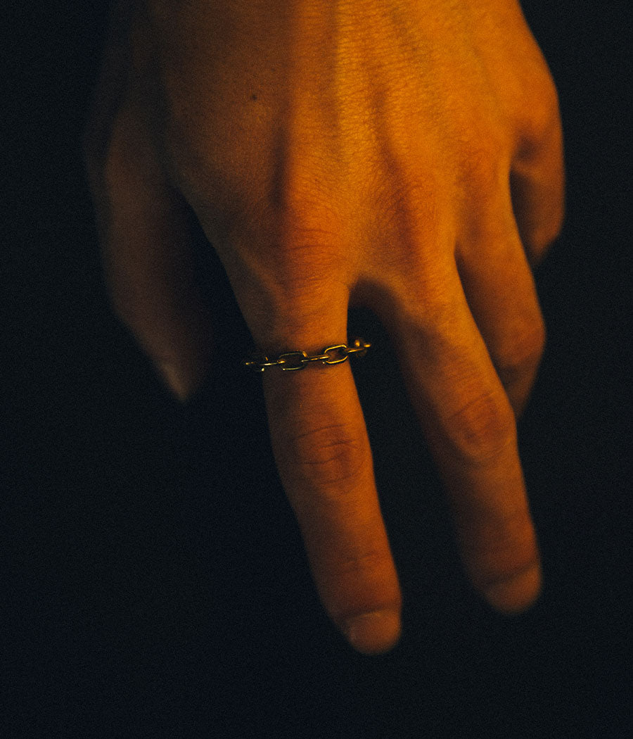 Hand wearing a gold ring on a dark background
