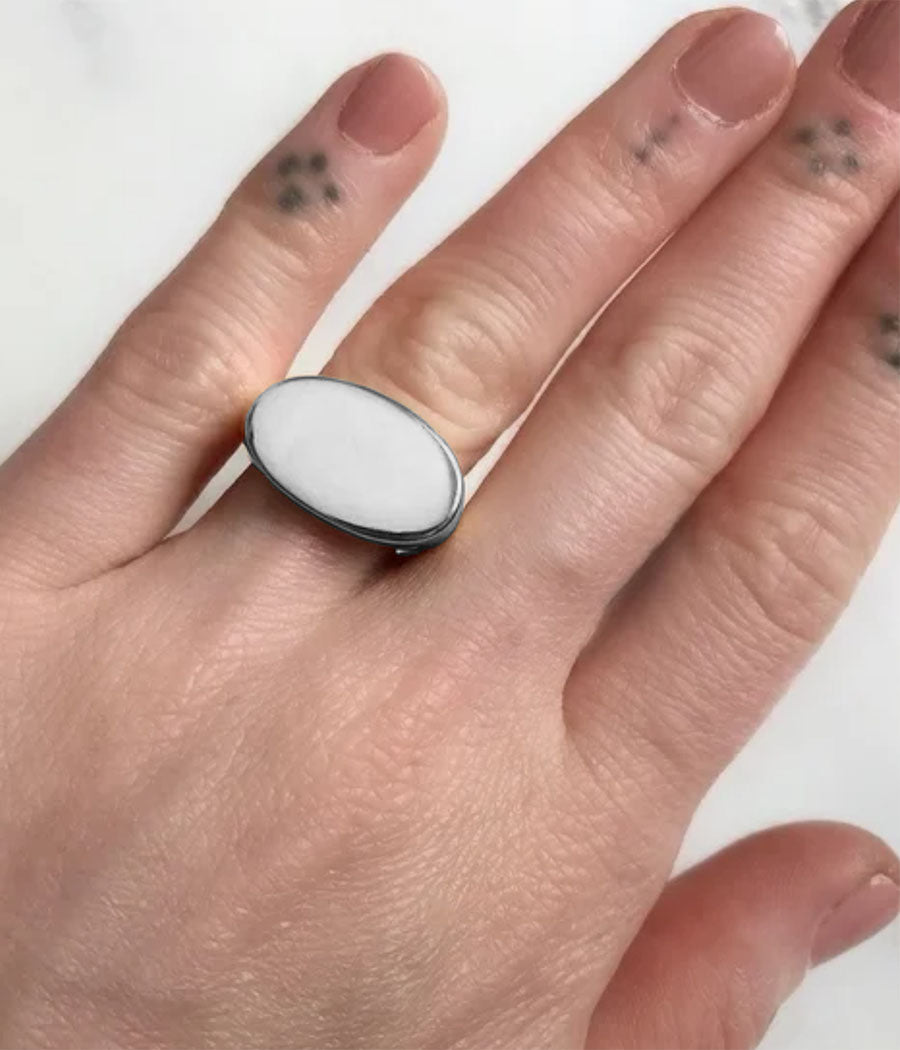 Hand wearing a ring with a white stone on a plain background