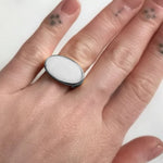 Hand wearing a ring with a white stone on a plain background