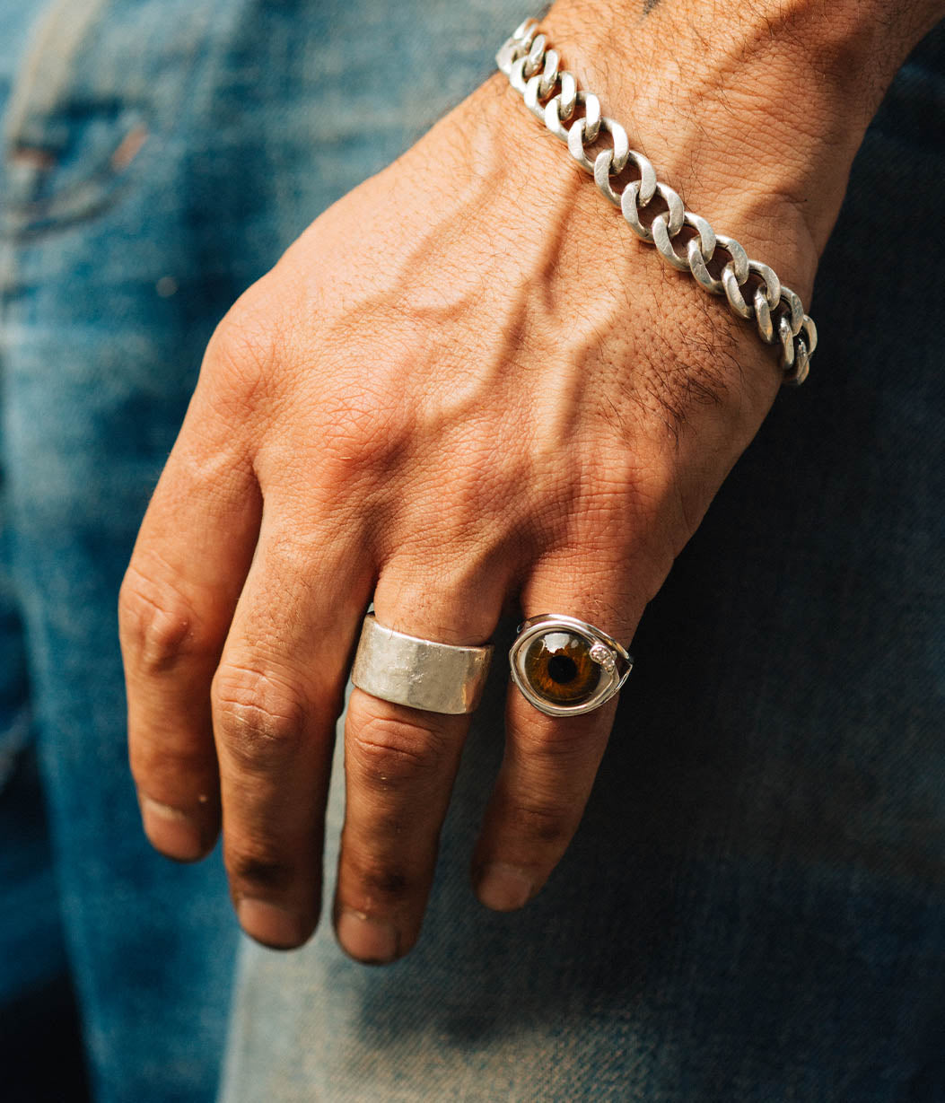 Hand wearing a silver ring and bracelet on a denim background