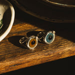 Two eye-shaped rings on a wooden surface with a dark background