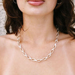 Silver chain necklace worn by a person with a neutral background