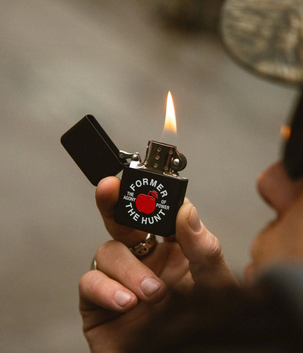Hand holding a zippo lighter with a visible flame against a neutral background