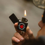 Hand holding a zippo lighter with a visible flame against a neutral background