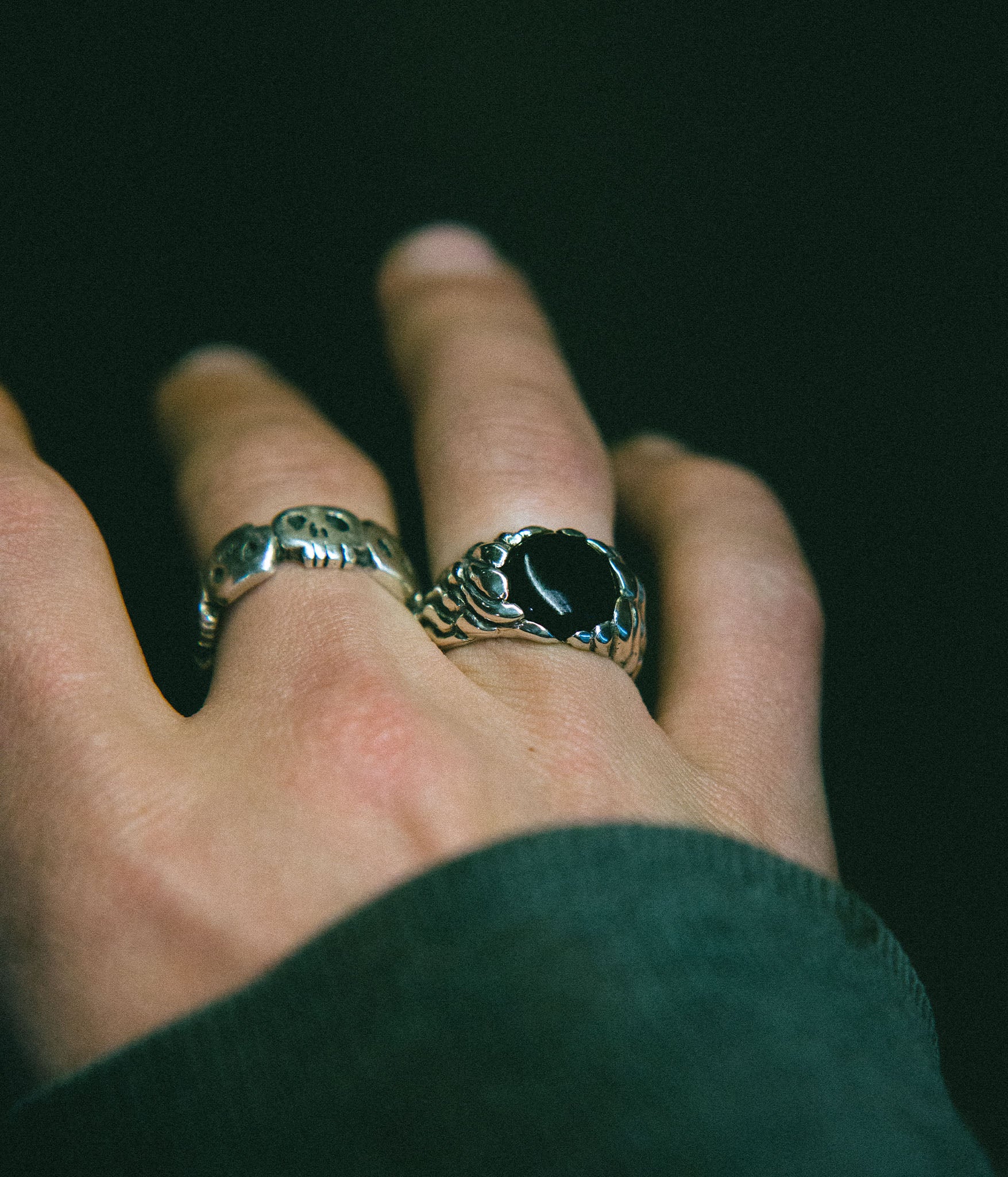 Hand wearing two rings with a dark background
