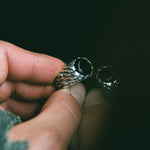Hand holding a silver ring with intricate design against a dark background