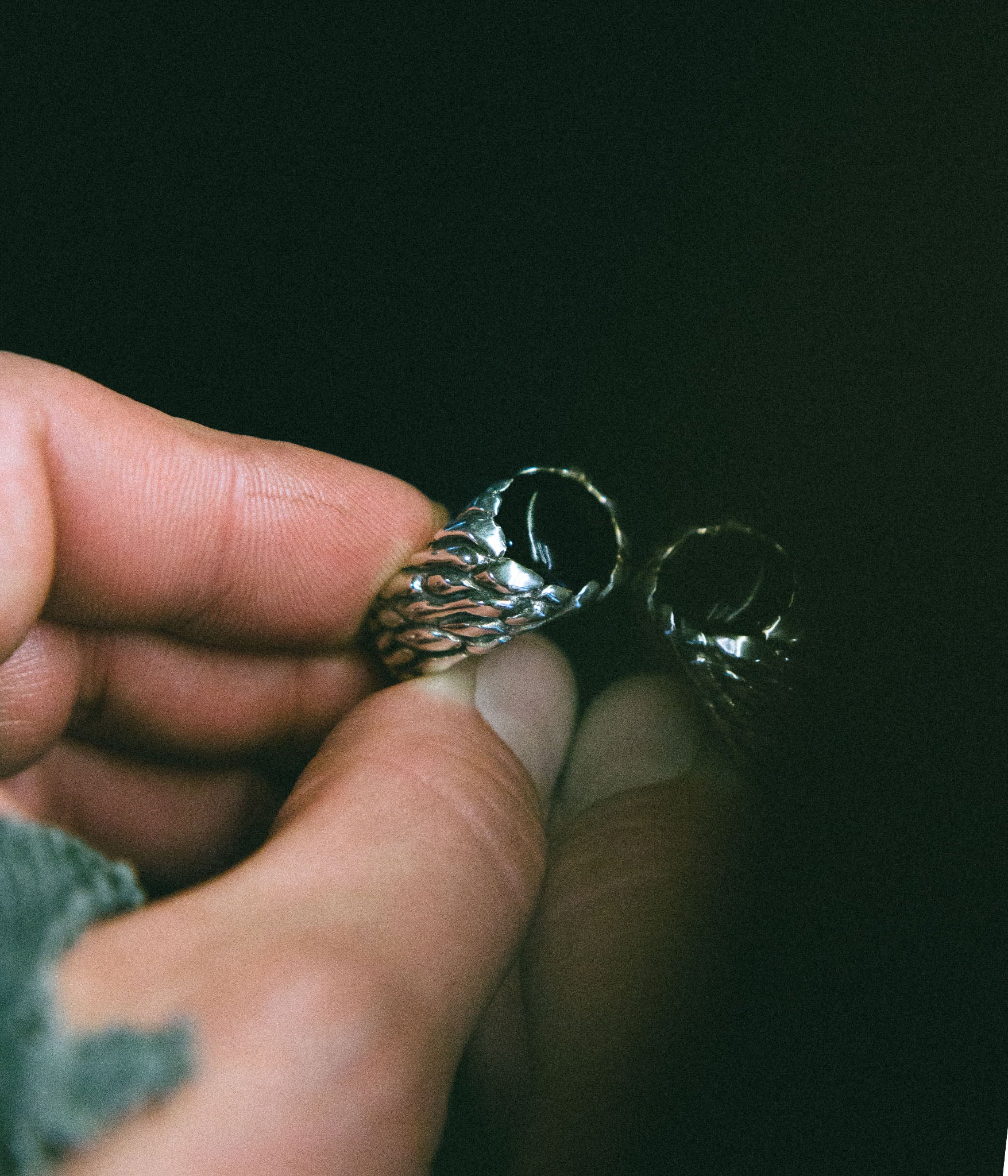 Hand holding a silver ring with intricate design against a dark background