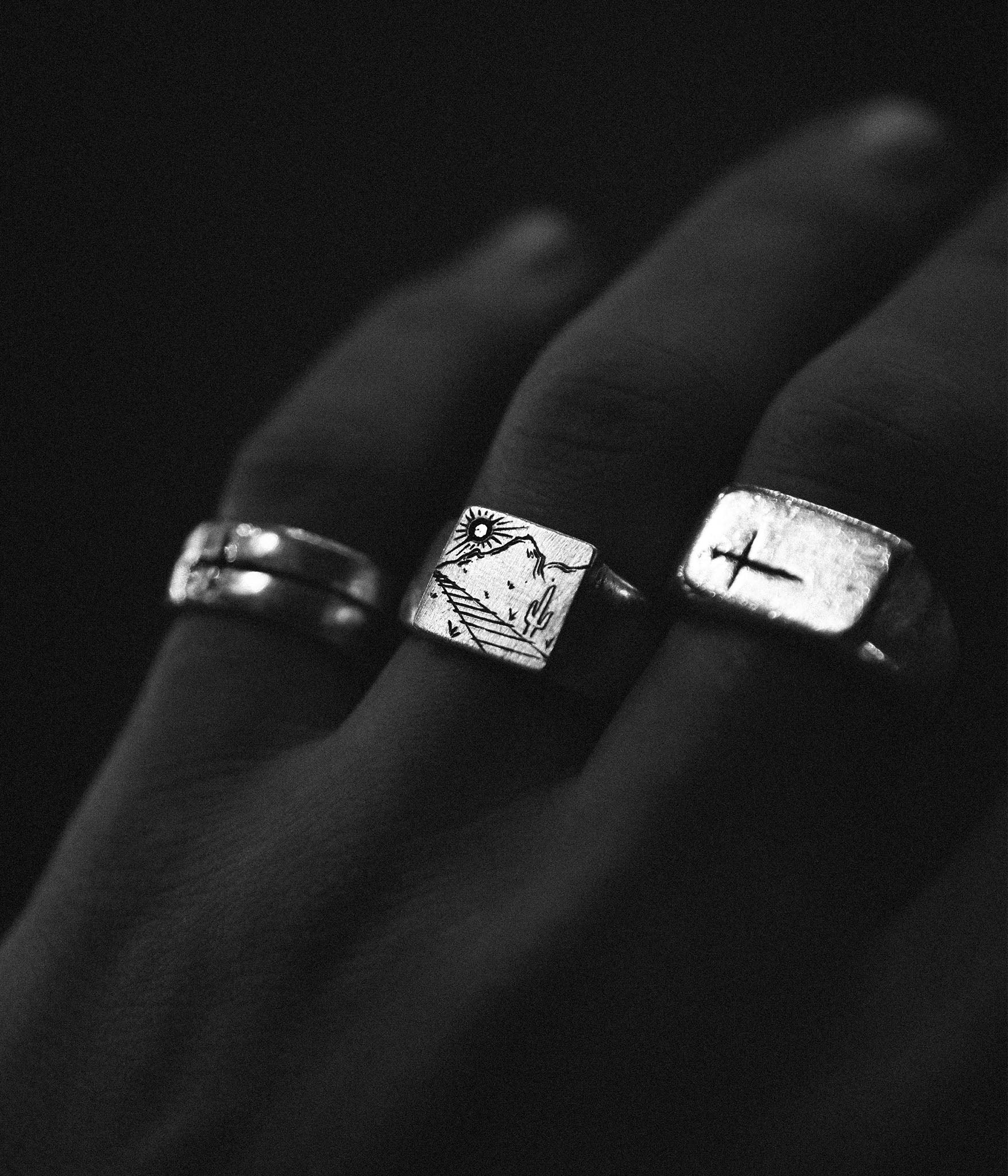 Three silver rings with unique designs on a dark background