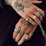 Hand with tattoos wearing multiple gold rings on a dark background