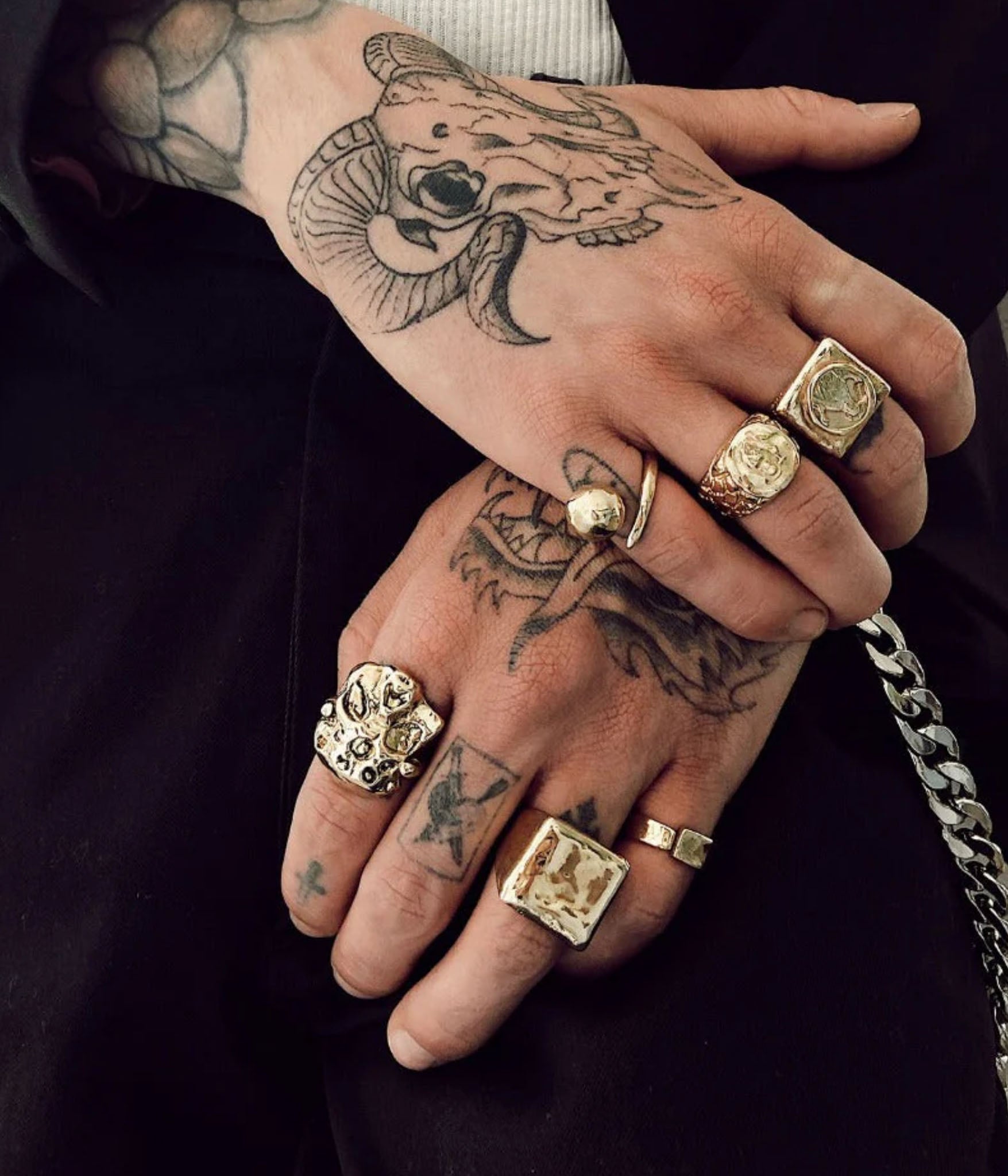 Hand with tattoos wearing multiple gold rings on a dark background